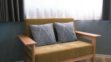 A chair with a cushion and a wooden armrest, positioned in a room with a window and curtains.