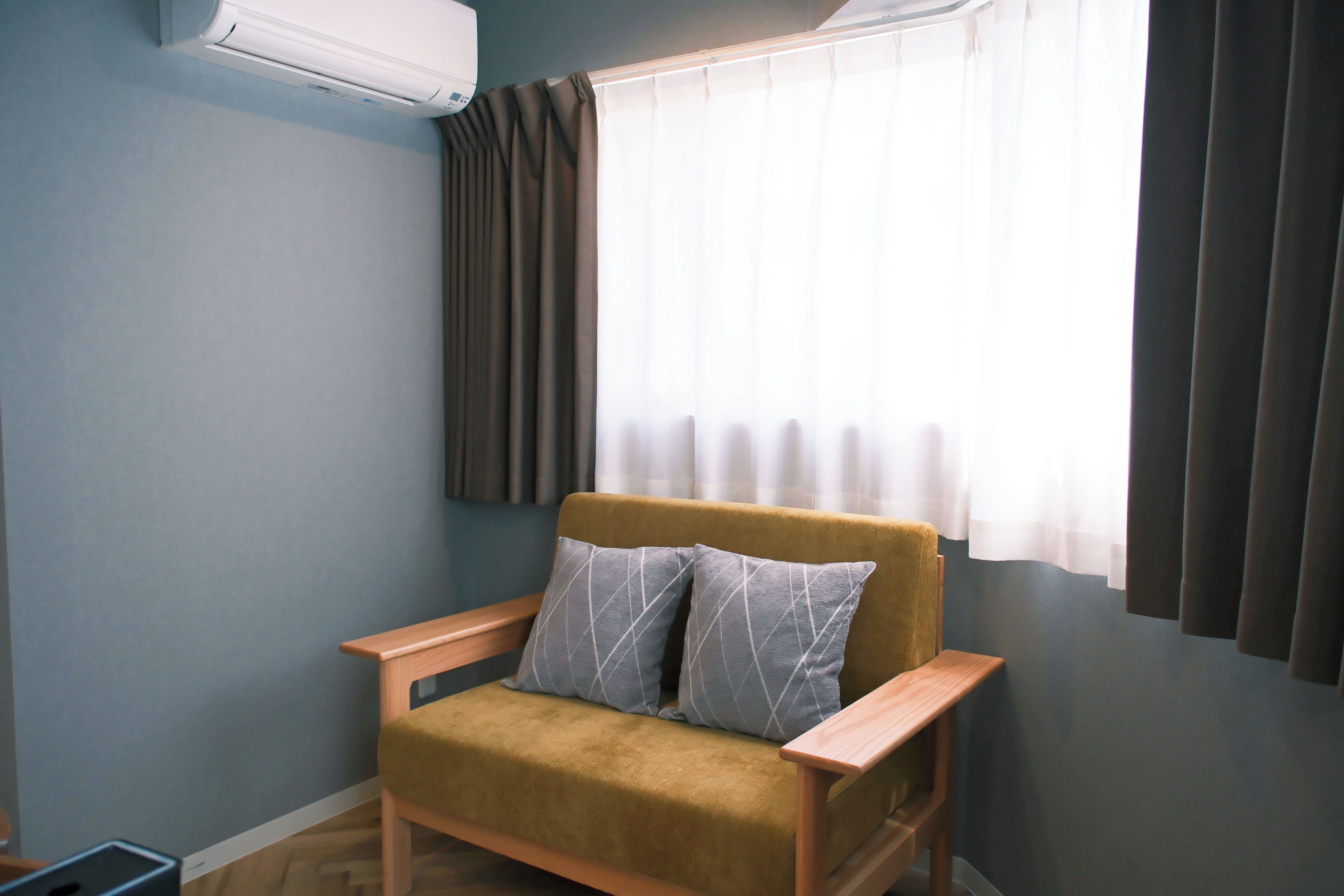 Quarto com um sofá, uma janela com cortinas e um aparelho de ar condicionado.