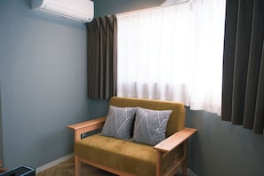 Quarto com um sofá, uma janela com cortinas e um aparelho de ar condicionado.