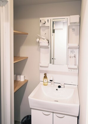 Casa de banho com lavatório branco, espelho, secador de cabelo e um cesto de lixo.