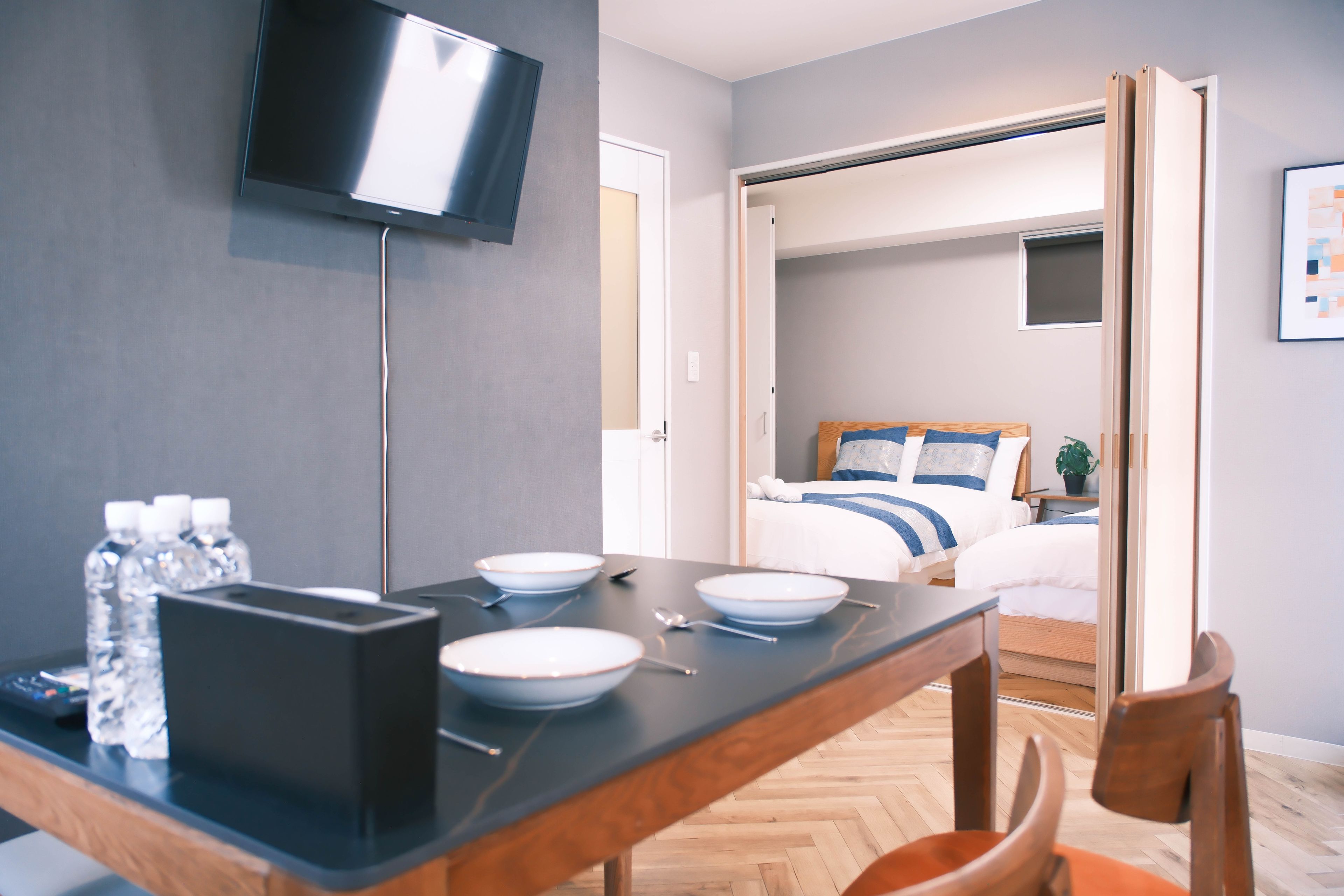 Quarto de hotel com cama, televisão presa na parede, mesa de jantar com pratos e tigela, e uma cadeira.