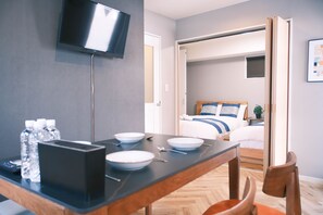 Een hotelkamer met een bed, een aan de muur bevestigde televisie, een eettafel met borden en een kom, en een stoel.