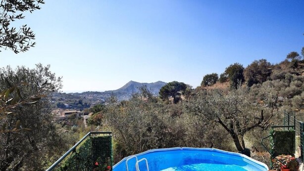 An outdoor swimming pool with a wooden deck, surrounded by trees and a mountain view. - Il Frantoio (Massa Lubrense)