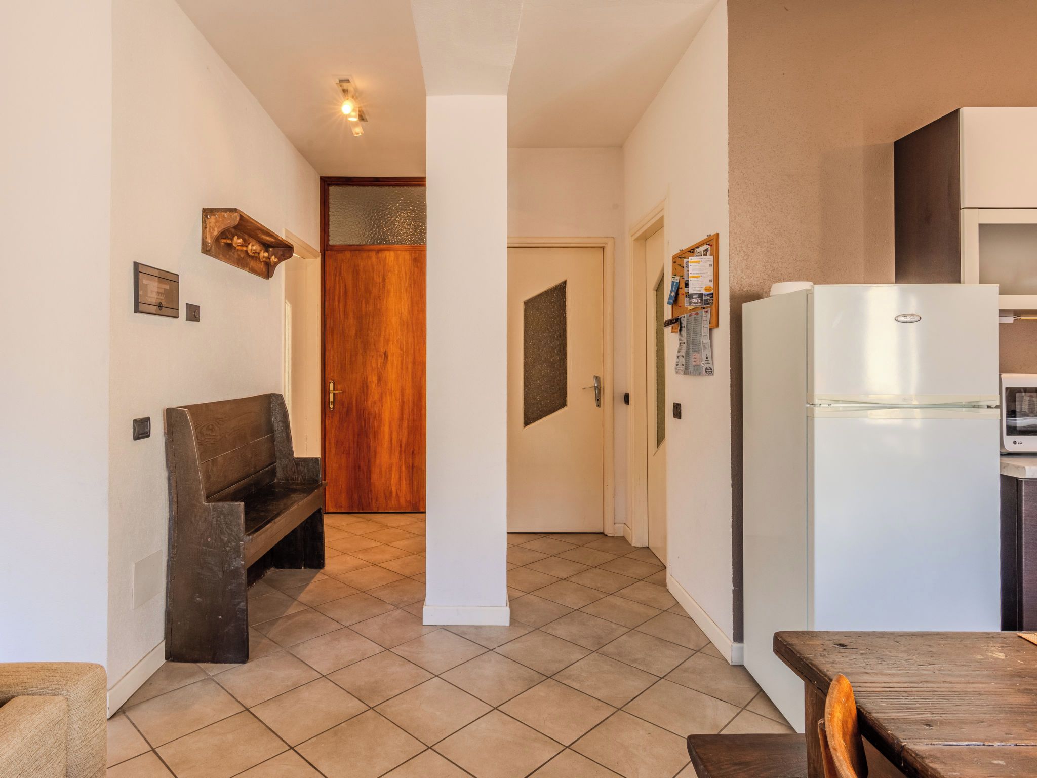 Una cocina con un refrigerador blanco, un banco de madera y un piso de baldosas.