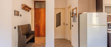 A kitchen with a white refrigerator, a wooden bench, and a tiled floor.
