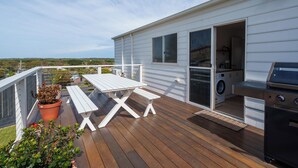 Une terrasse avec une table et des chaises, un barbecue et une machine à laver visibles à travers une porte ouverte.