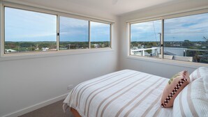 Une chambre à coucher avec un lit, deux fenêtres, un ventilateur de plafond et une vue sur la ville.