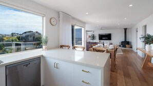 Une cuisine moderne équipée d’un lave-vaisselle, un coin repas avec une table pour quatre personnes, et un salon avec un canapé et un téléviseur.