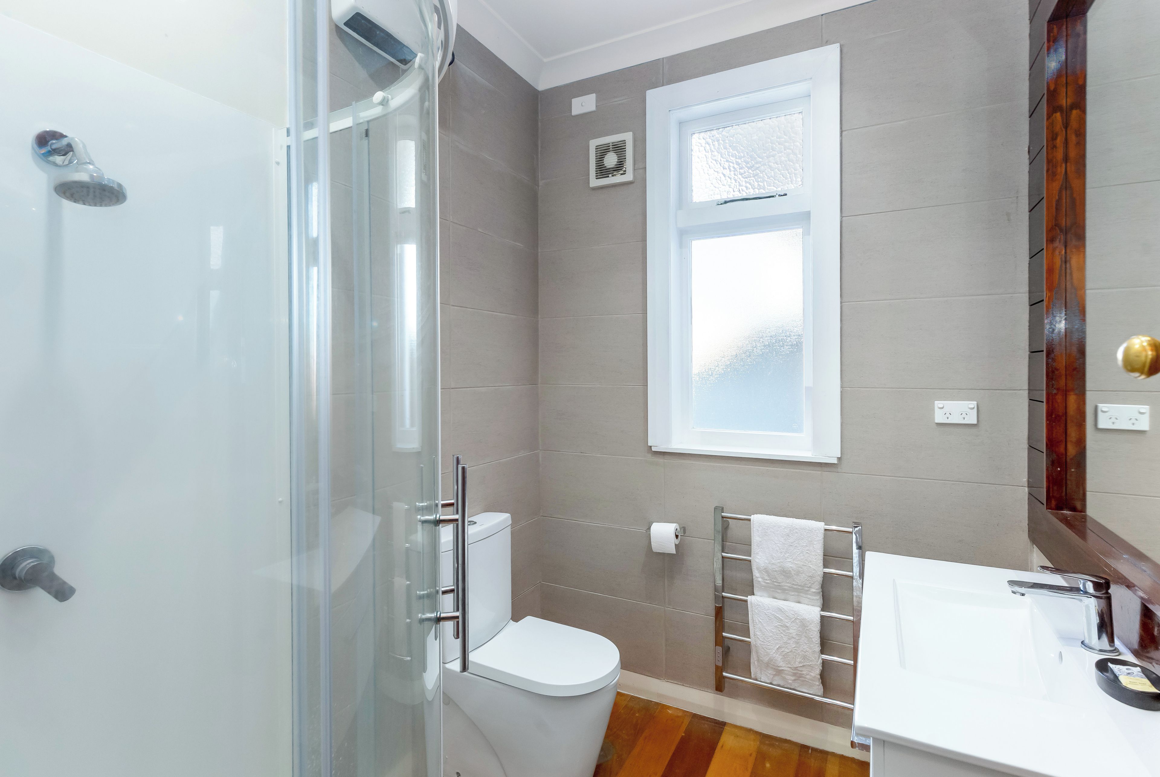 A modern bathroom with a glass shower enclosure, a toilet, a sink with a mirror, and a towel rack.