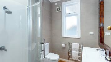 A modern bathroom with a glass shower enclosure, a toilet, a sink with a mirror, and a towel rack.