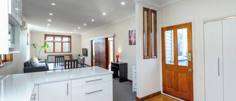 A modern kitchen with white cabinetry, a dining area with a table and chairs, and a wooden floor.