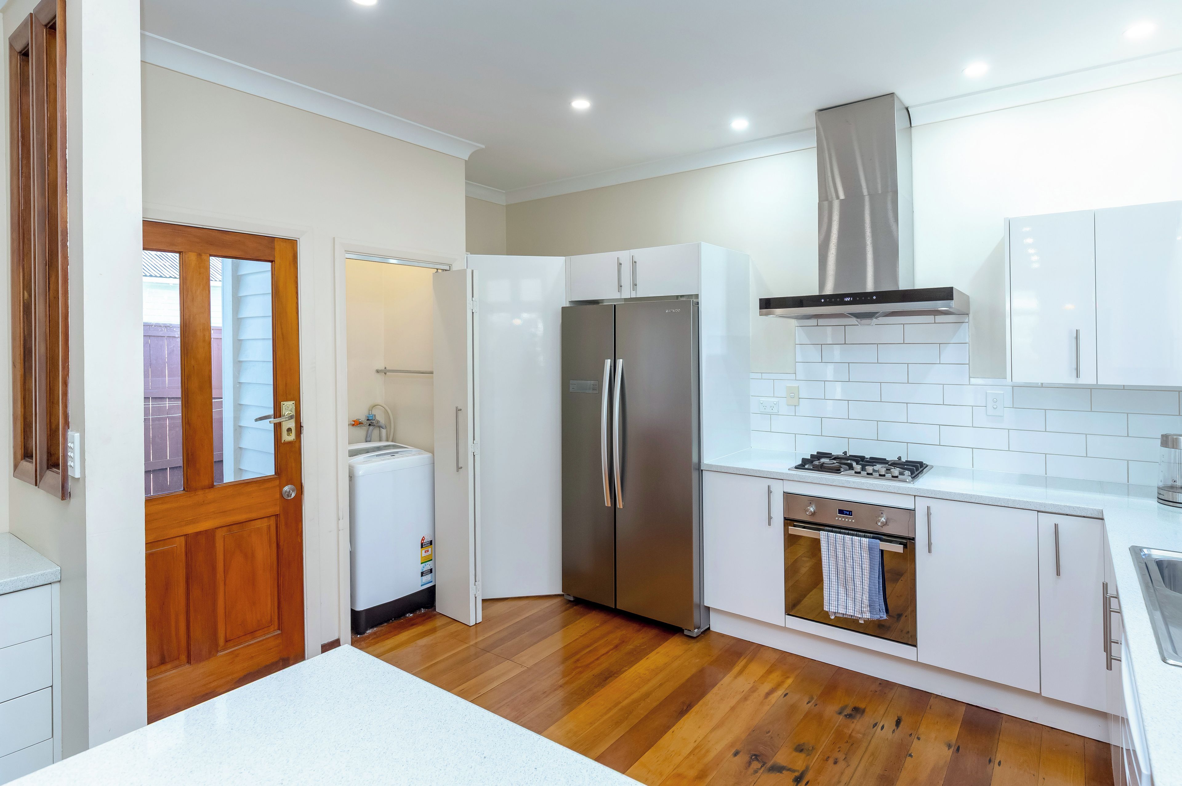 A compact kitchen with white cabinets, a stainless steel refrigerator, a built-in oven, and a gas stove.