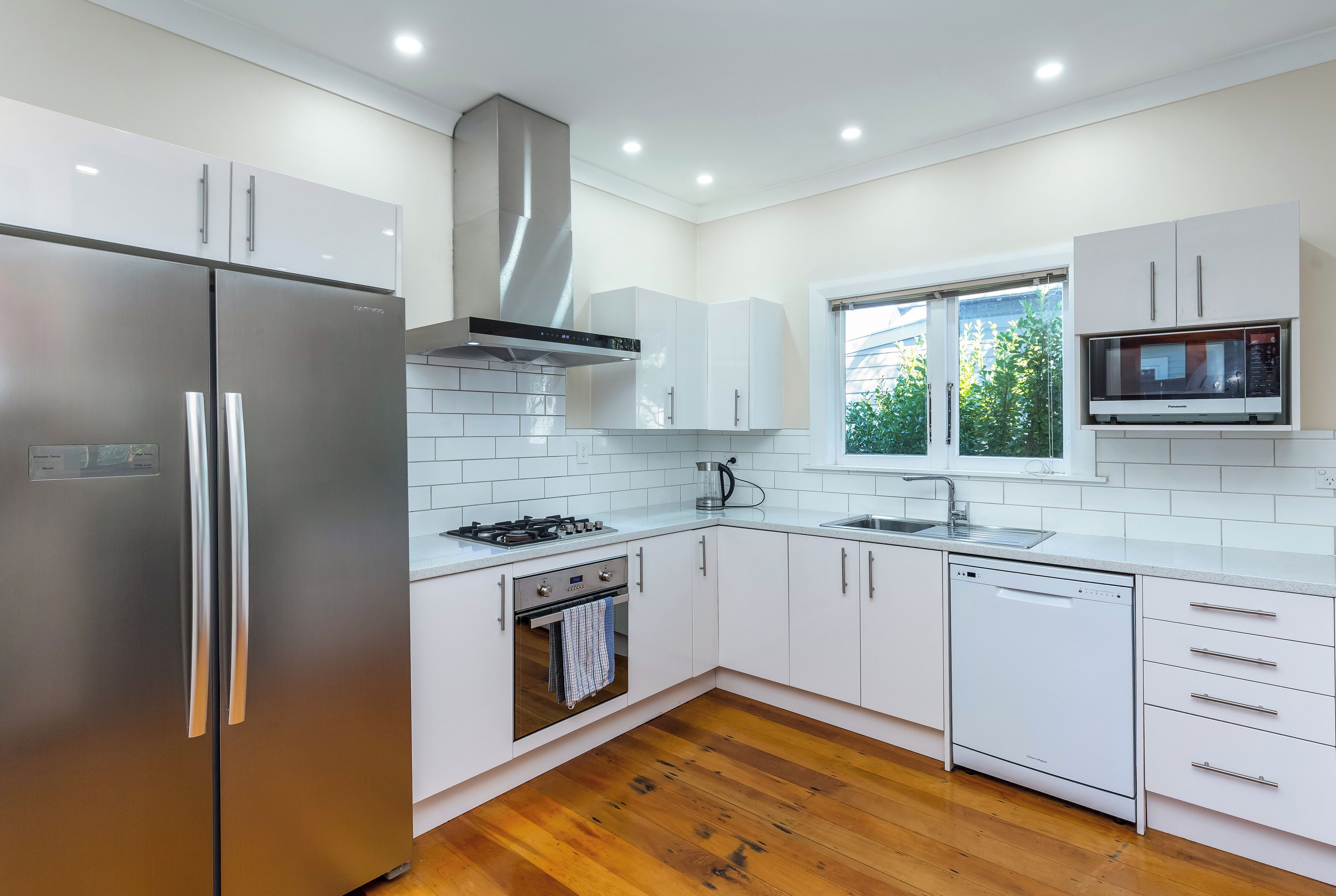 Una cocina moderna con electrodomésticos de acero inoxidable, armarios blancos y piso de madera.