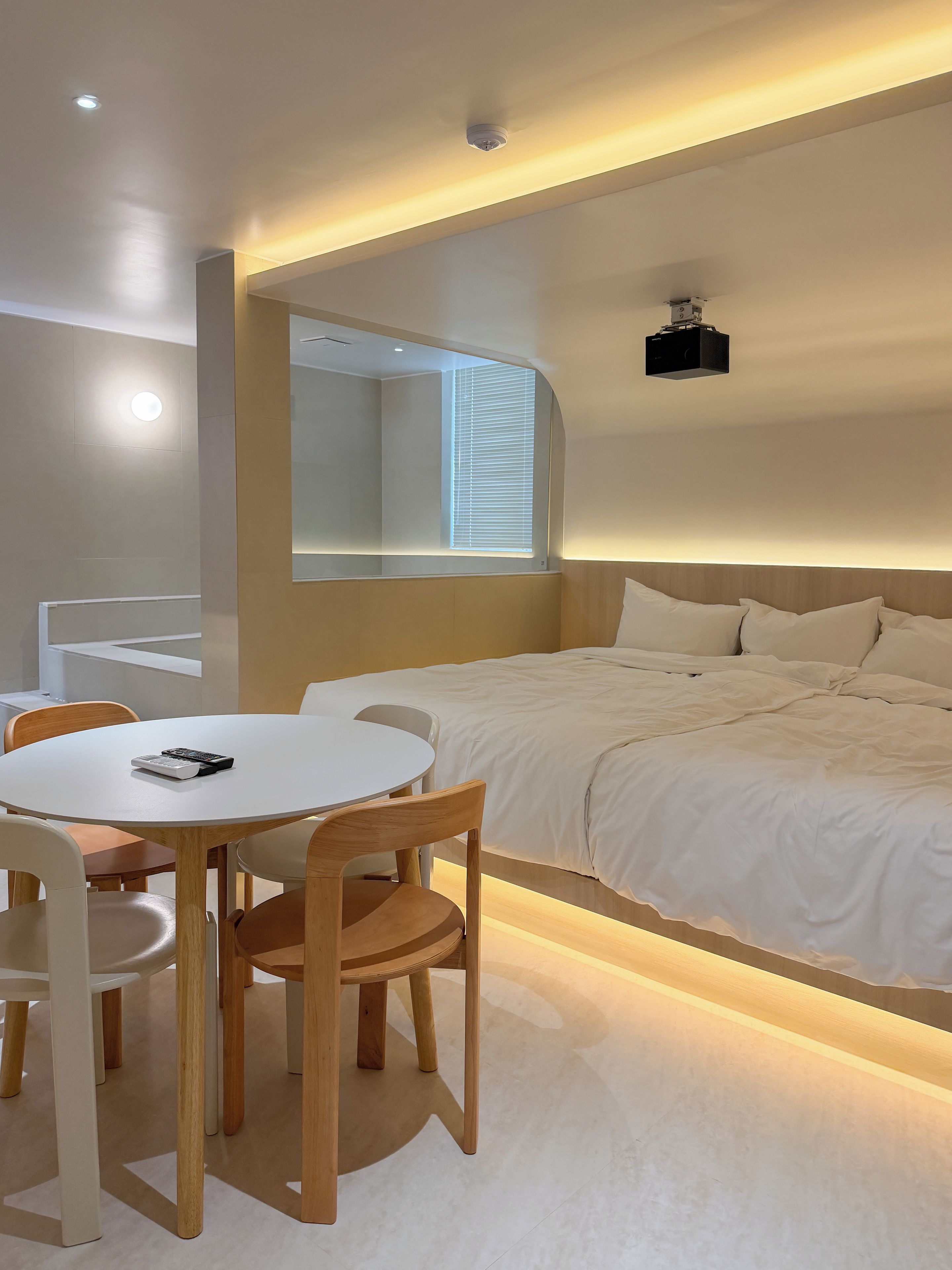 Une chambre moderne avec un lit, une table de chevet et une table à manger ronde, accompagnée de chaises.
