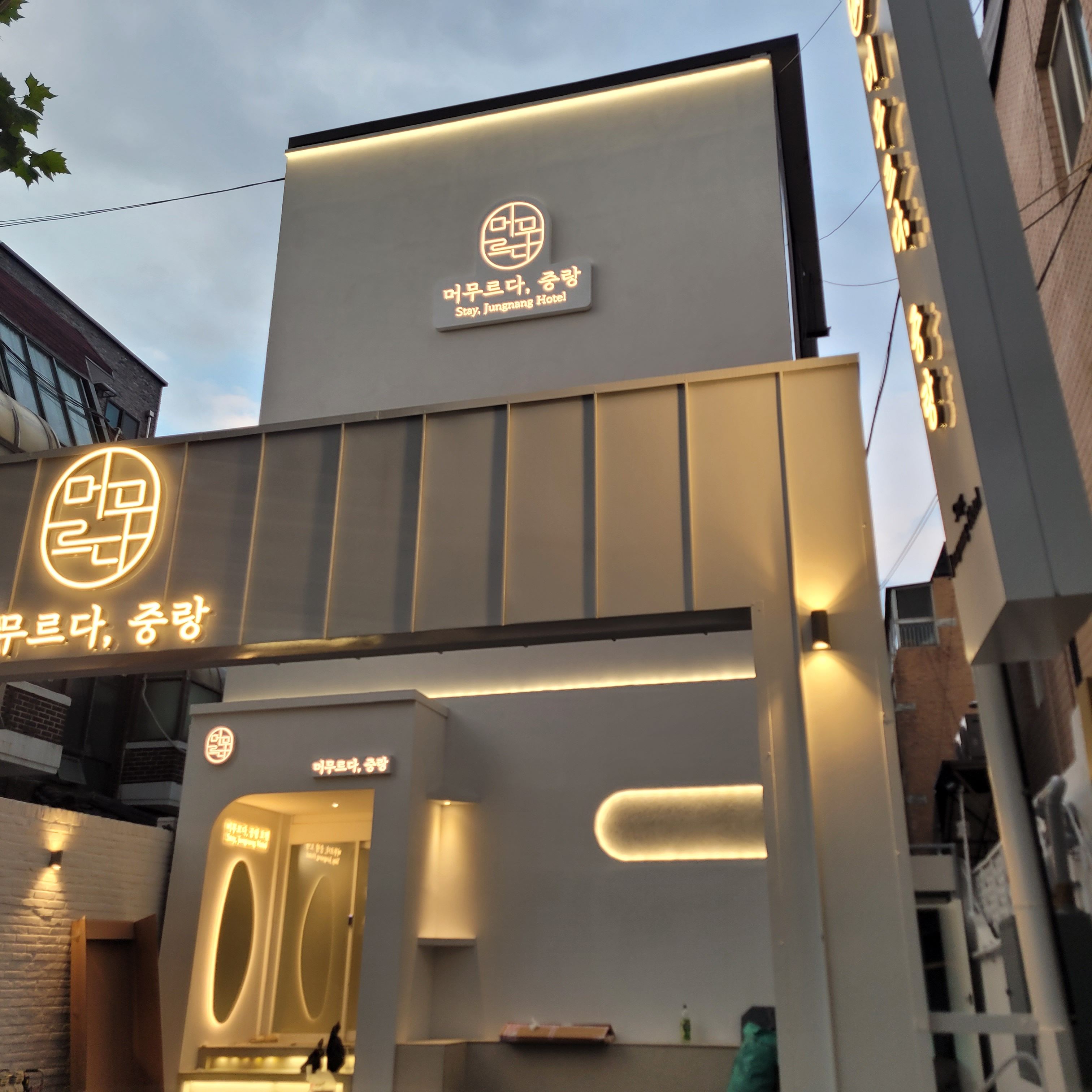 A modern hotel facade with illuminated signage, a reception area, and a visible entrance.