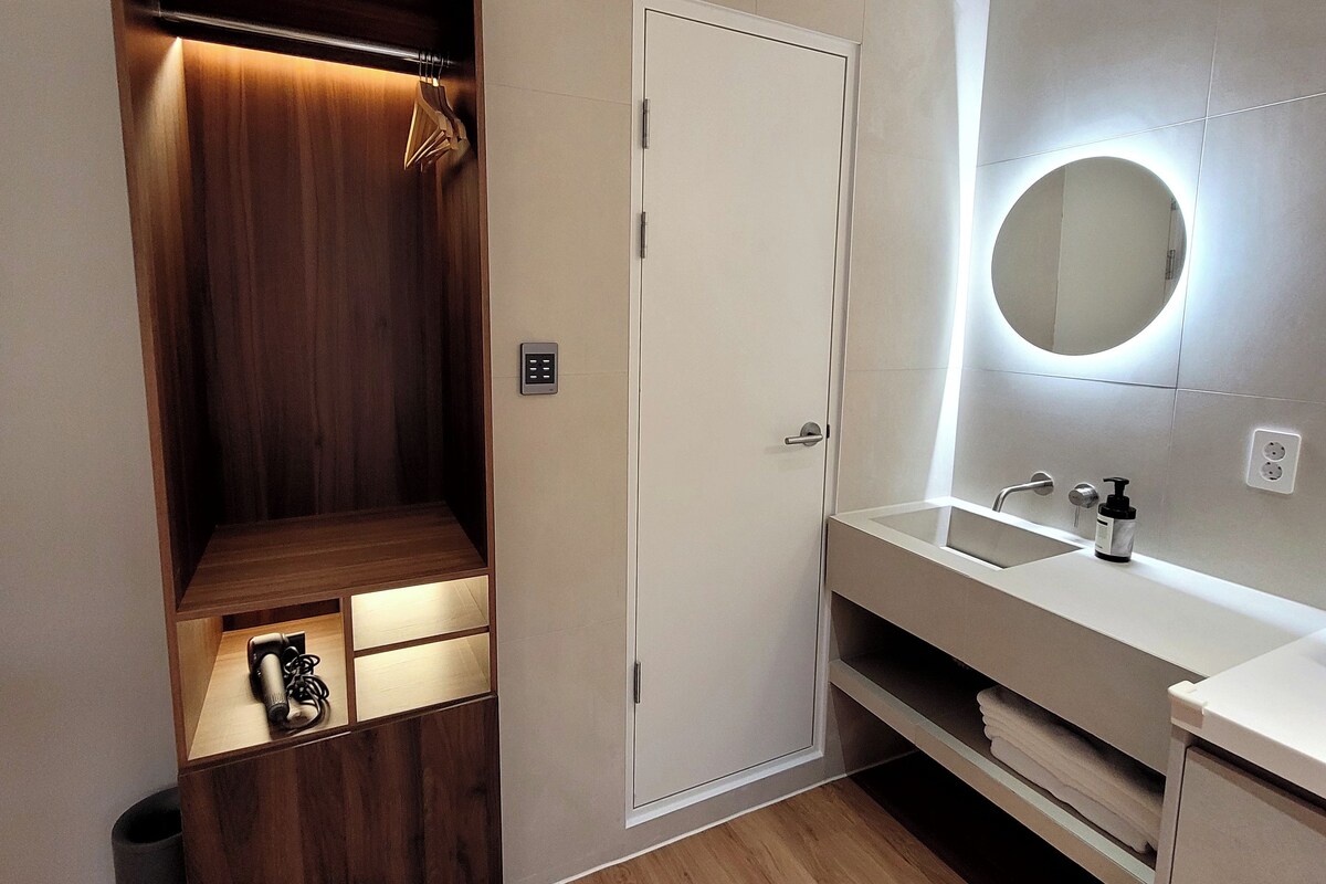 A modern bathroom with a wooden vanity, a white sink, and a mirror with a circular light.
