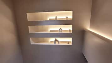 A room with a recessed shelf unit against the wall, a ceiling-mounted security camera, and a digital clock on the floor.
