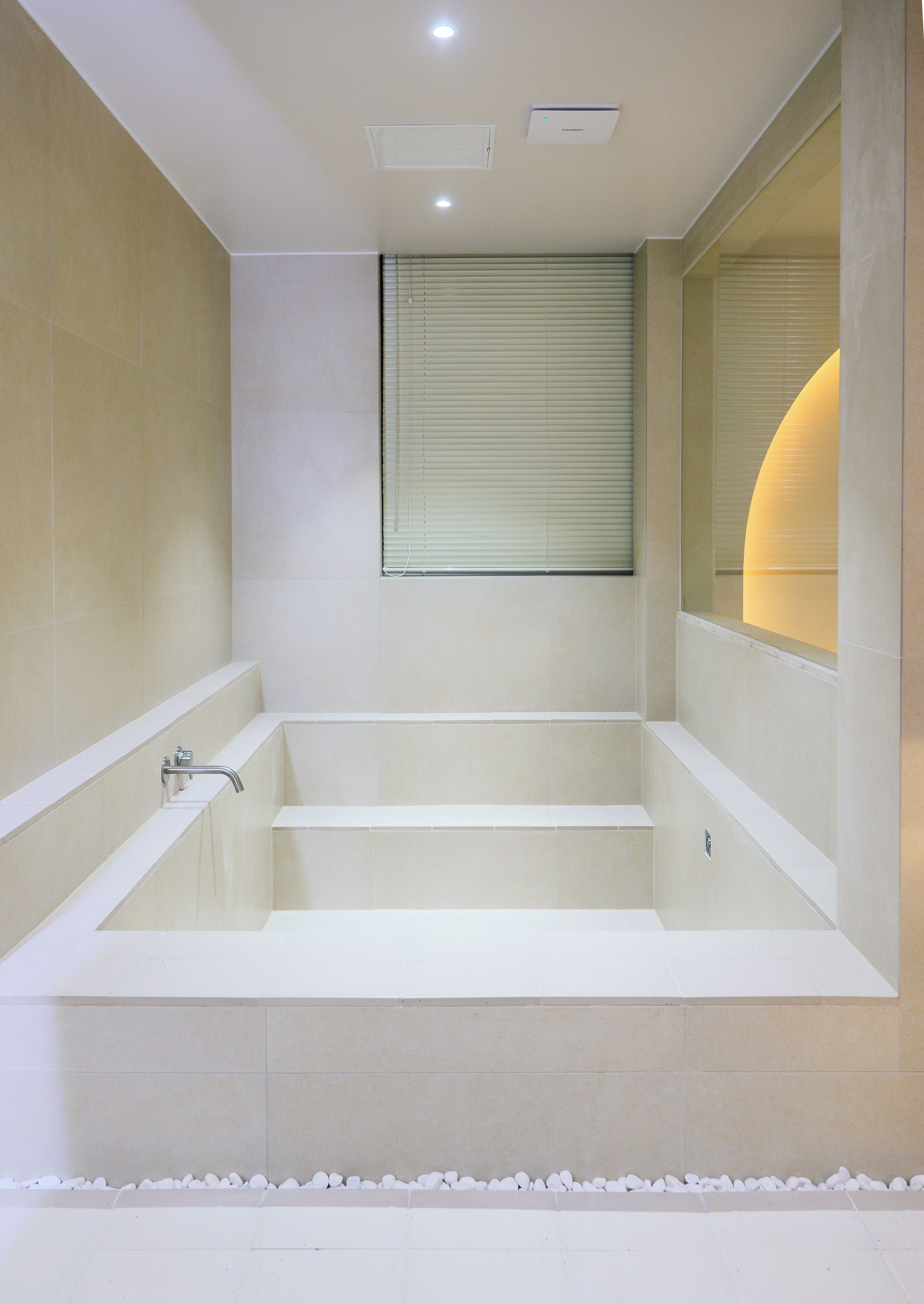 A modern bathroom with a large bathtub, a window with blinds, and a ceiling light fixture.