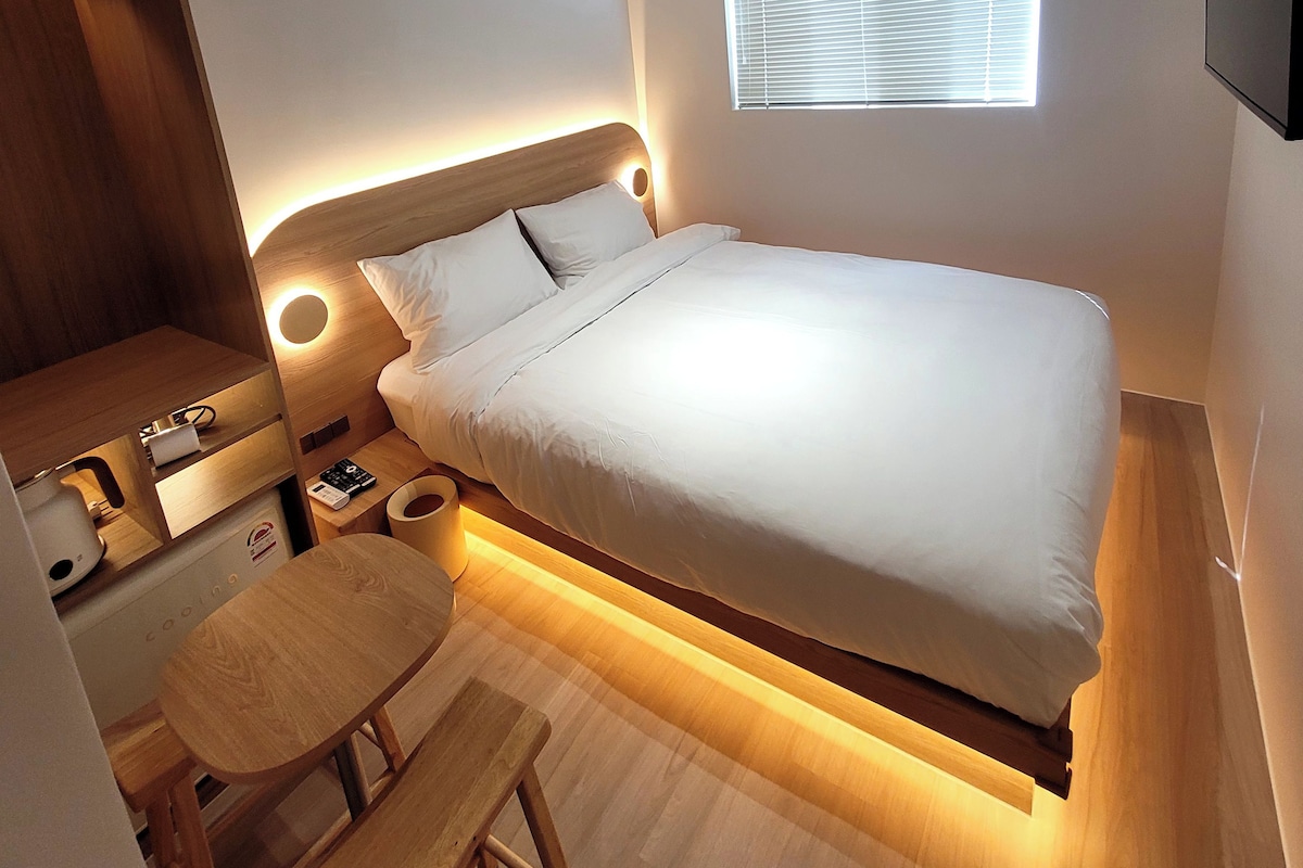 Une chambre à coucher moderne avec un lit, une table de chevet, une lampe et un petit banc en bois.