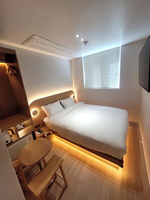 Une chambre à coucher moderne avec un lit, une table de chevet, une lampe et un petit banc en bois.