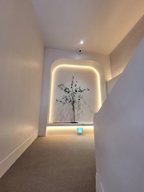 A modern interior with a minimalist design, featuring a recessed wall with a tree sculpture and a lit exit sign.