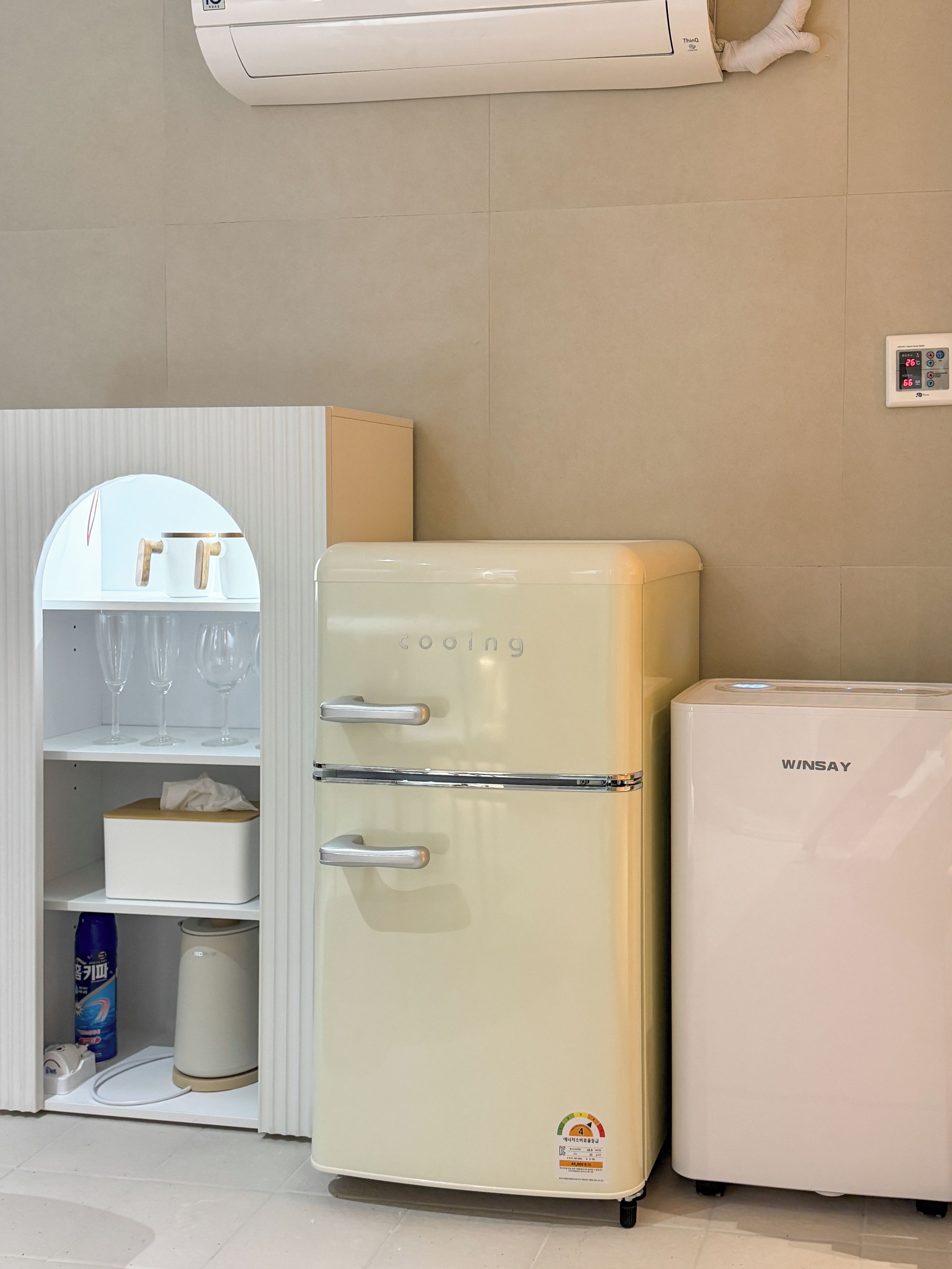 A vintage Winsay refrigerator next to a modern one, both in a kitchen with a white cabinet and a mirror.