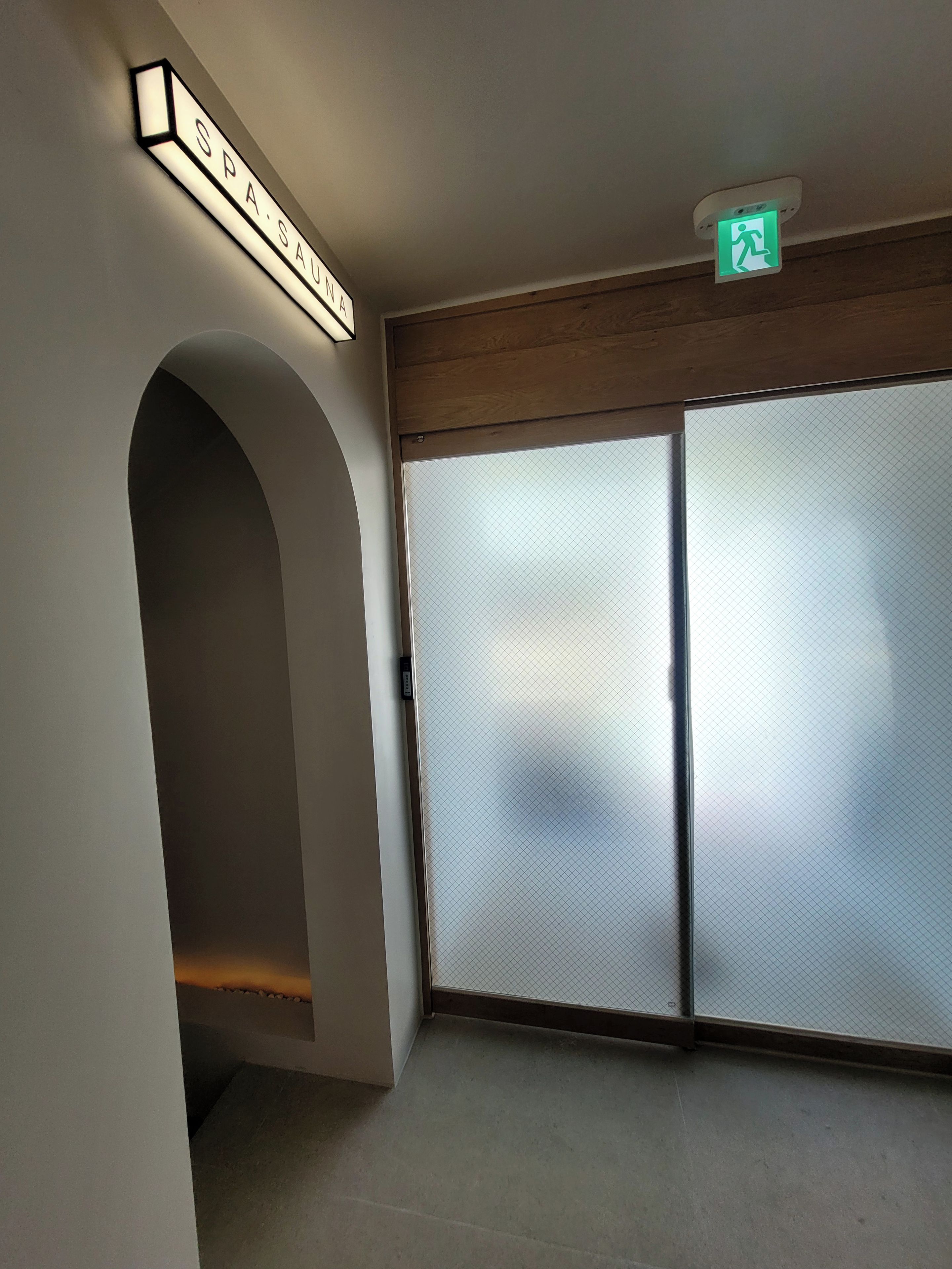 A hallway with a spa sign, a green emergency exit sign, and a sliding glass door.