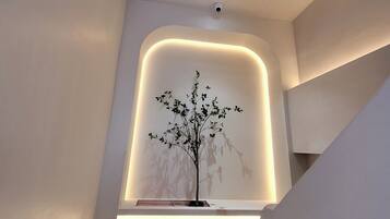 A modern interior with a minimalist design, featuring a recessed wall with a tree sculpture and a visible exit sign.