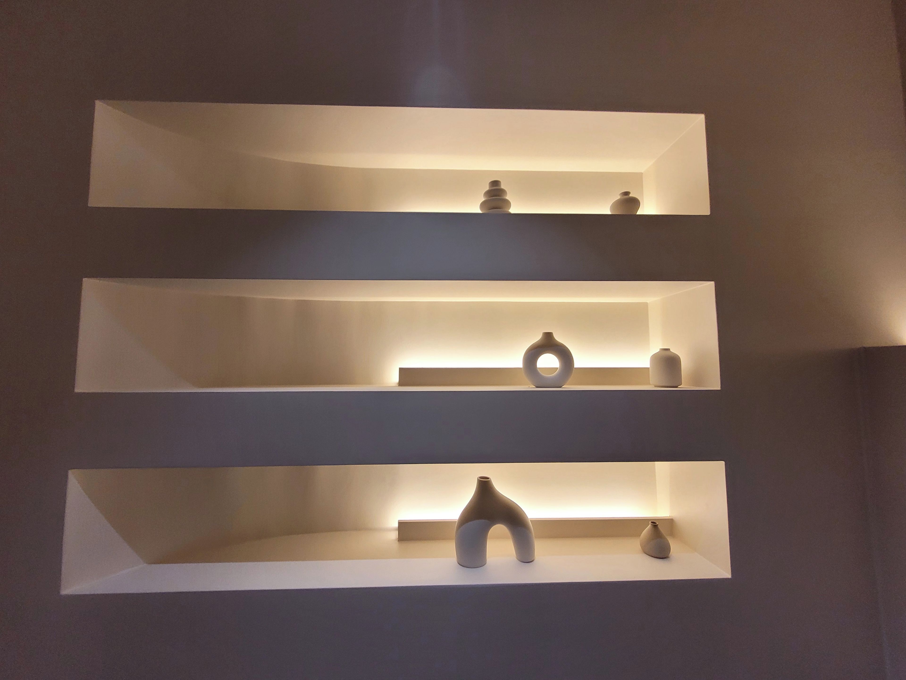 Three white shelves with various ceramic objects.