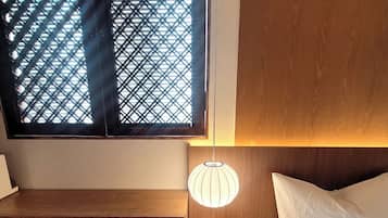 Un dormitorio con una cama, una mesita de noche, una lámpara de pared y una ventana con diseño de celosía.