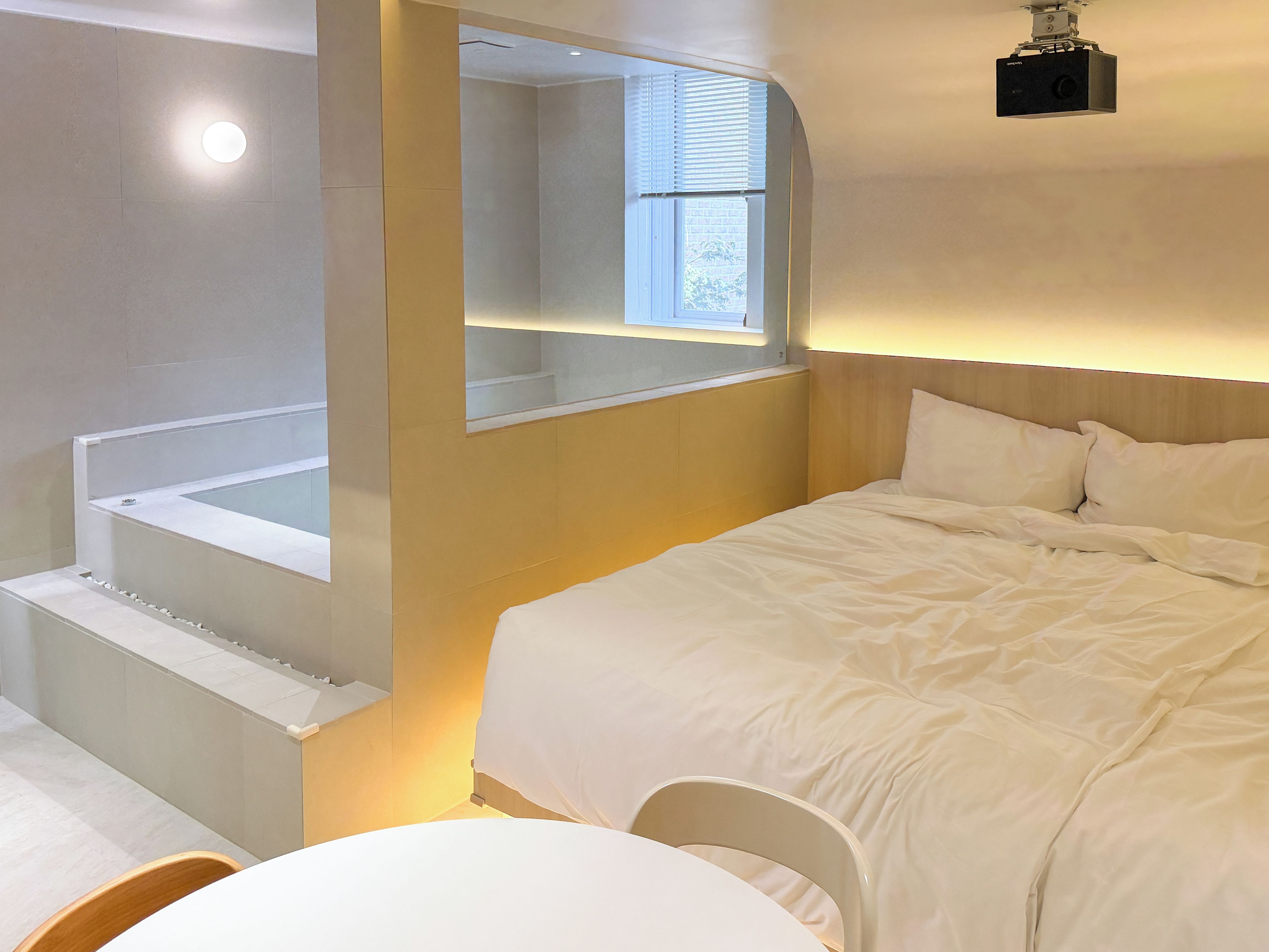 A modern hotel room with a large bed, a small table, and a bathtub.
