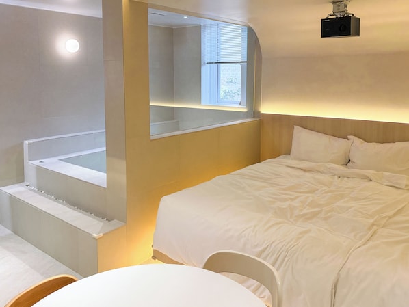 A modern hotel room with a large bed, a small table, and a bathtub.