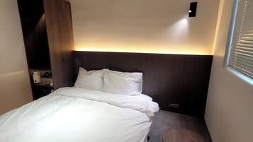 A hotel room with a bed, bedside table, and a wall-mounted air conditioning unit.