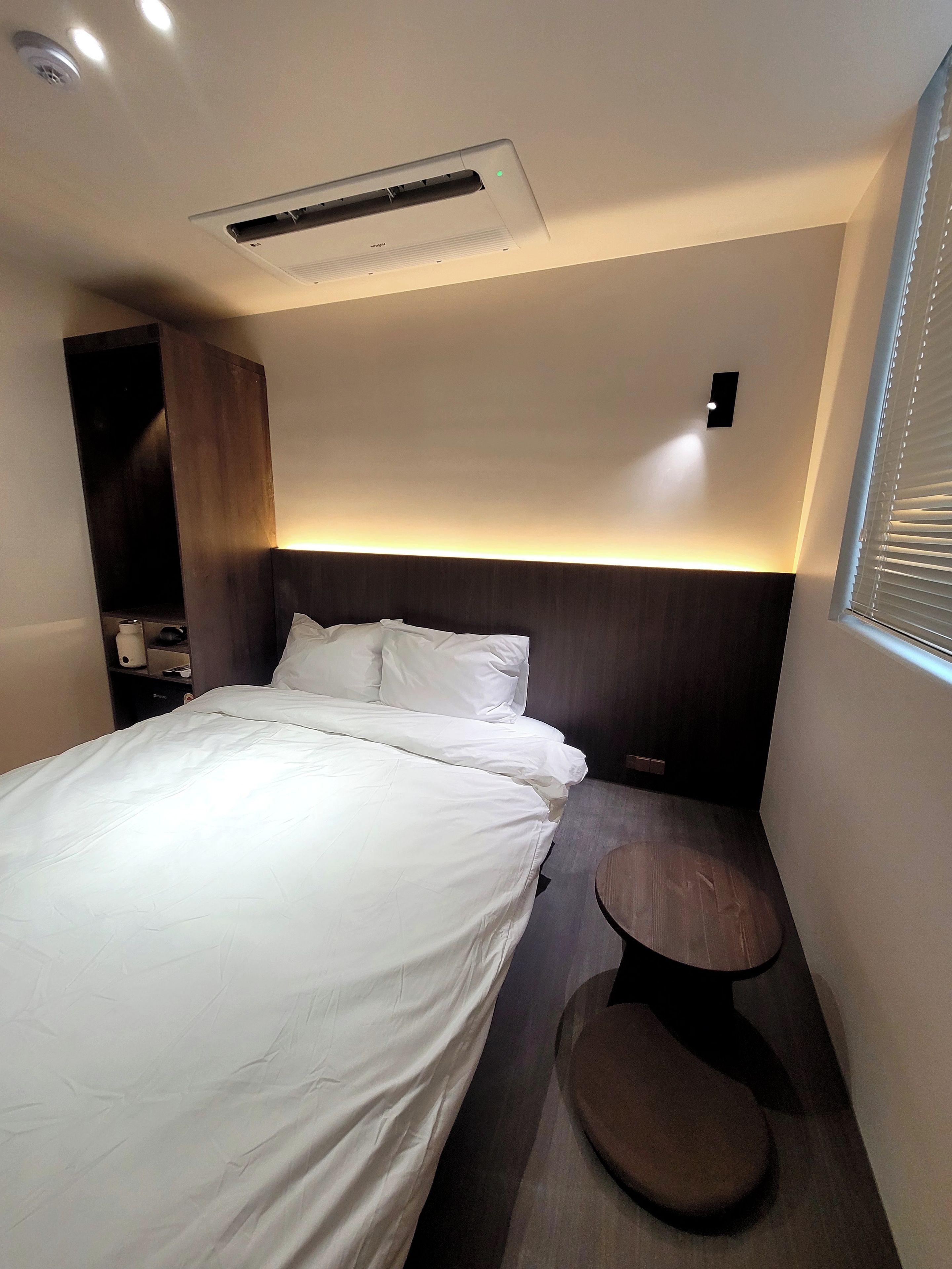 A hotel room with a bed, bedside table, and a small seating area.