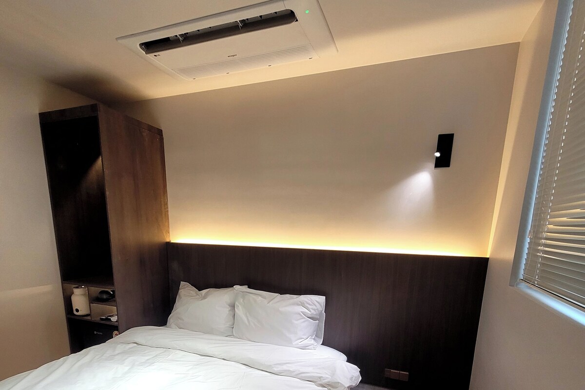 A hotel room with a bed, bedside table, and a small seating area.