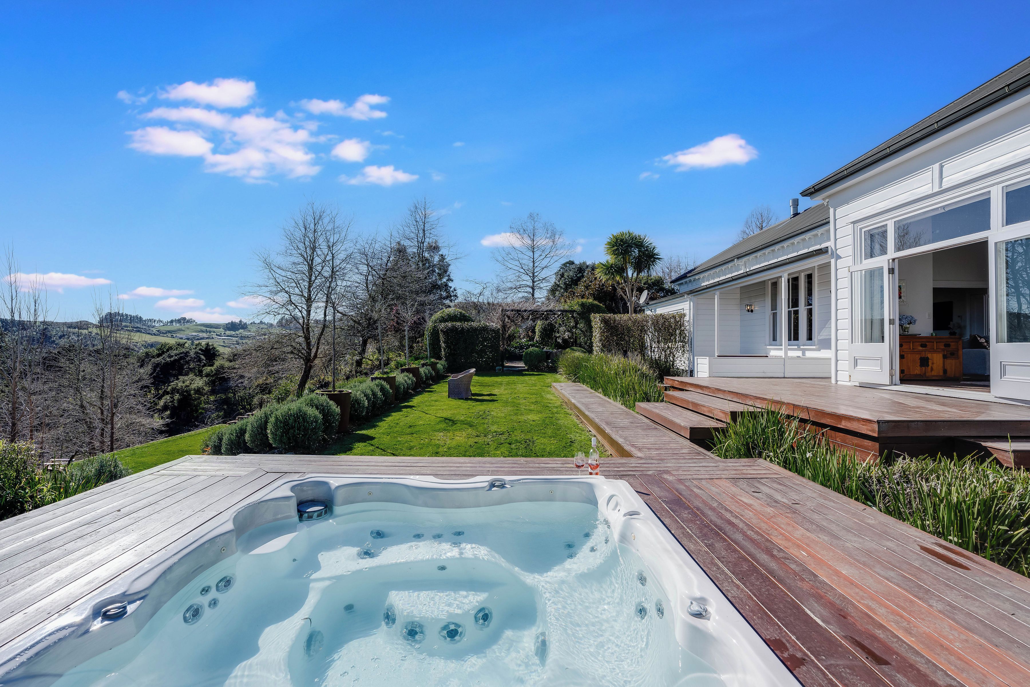 A hot tub with a wooden deck, a grassy lawn, and a house with large windows.