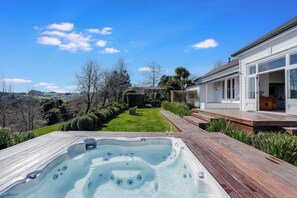 A hot tub with a wooden deck, a grassy lawn, and a house with large windows. - The An Chroi Estate by Homello (Bombay)