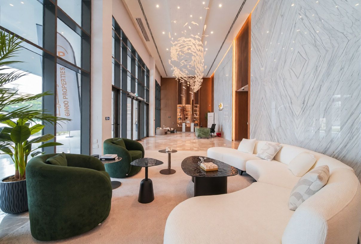 A modern lobby with a curved white sofa, green armchairs, and a large potted plant.