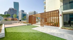 A modern outdoor area with artificial grass, a wooden pergola, and a cityscape view in the background. - Vogue | VYB at Business Bay close to Downtown (Dubai)