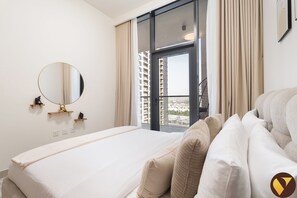 A hotel room with a bed, a round mirror, a window with curtains, and a view of a cityscape. - Vogue | VYB at Business Bay close to Downtown (Dubai)