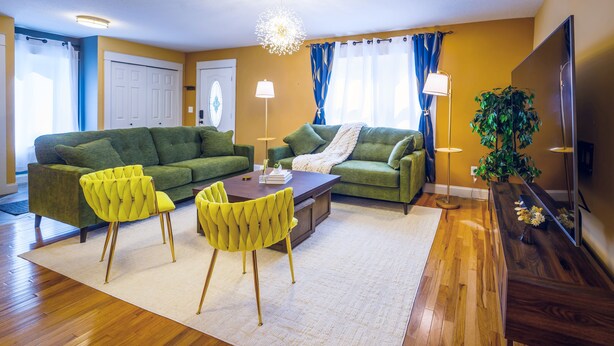 Una sala de estar con un sofá verde, sillas amarillas, una mesa de centro y un televisor sobre un mueble de madera.