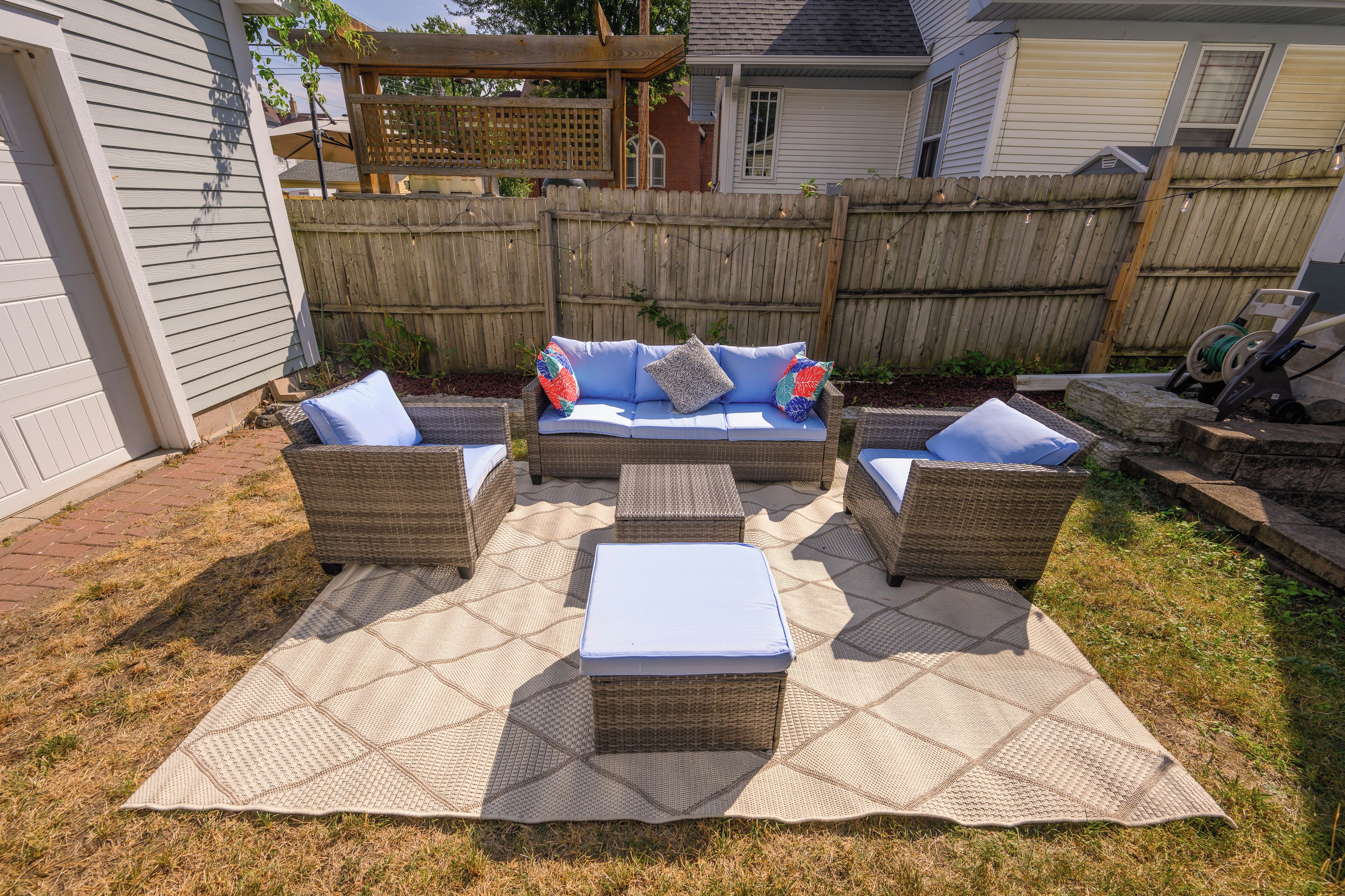Een terras buiten met rieten meubels en een geweven vloerkleed.