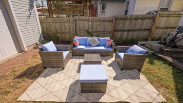 Een terras buiten met rieten meubels en een geweven vloerkleed.
