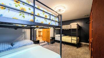 Een slaapzaal met stapelbedden, een plafondventilator en een deur naar een andere kamer.