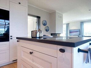 Une cuisine moderne avec des meubles blancs, un plan de travail foncé et une vue sur la ville grâce à de grandes fenêtres.