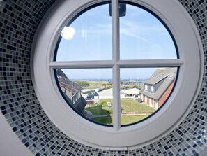 A circular window with a view of a residential area, including houses and a road. - Holiday Home Horsa Hoog (Wenningstedt-Braderup)