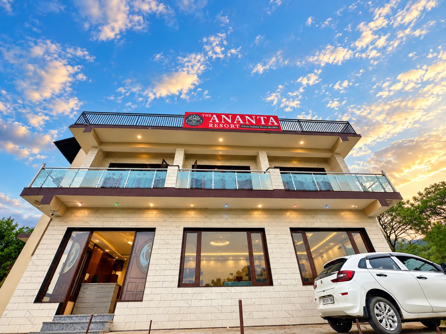 A hotel with a sign reading 'The Ananta Resort.' It has multiple floors, balconies with glass railings, and a white car parked in front.