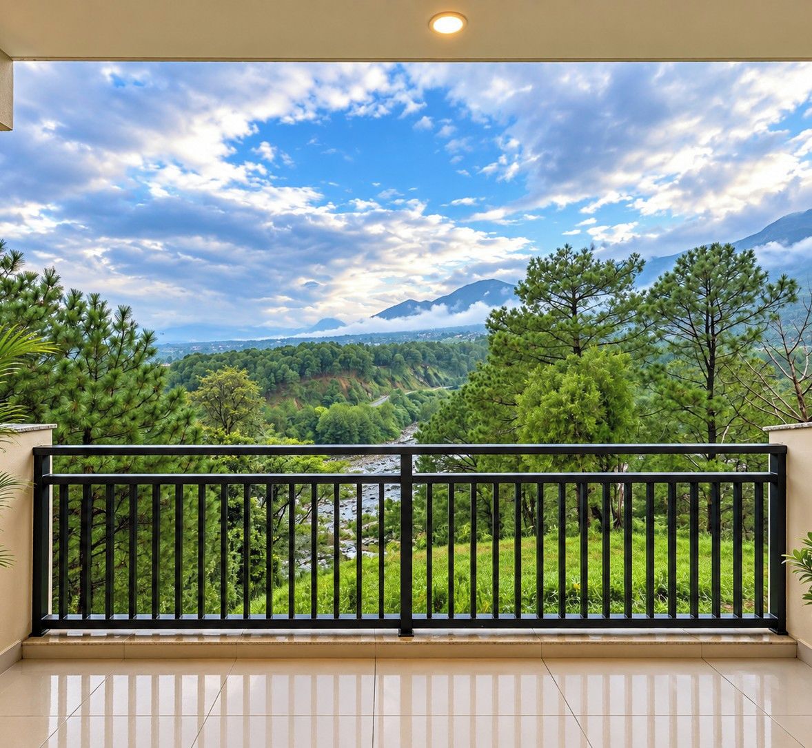 A balcony with a black railing overlooking a lush green landscape with trees and a mountain in the distance.