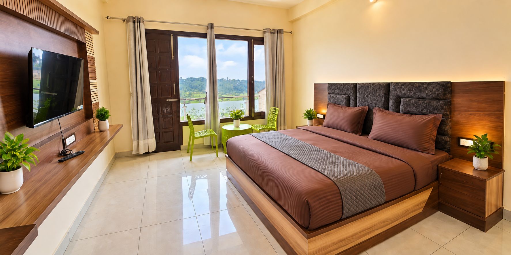 Quarto de hotel moderno com uma cama grande, televisão, varanda com vista e uma pequena mesa com cadeiras.