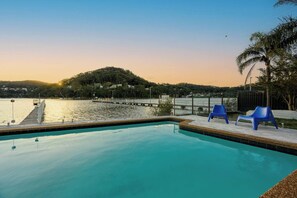 A swimming pool with a view of a dock and a hill in the background. - Waterfront Escape with Jetty and Pool (Woy Woy)